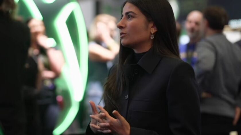 Xbox CEO Asha Sharma speaking at an Xbox event with the illuminated green Xbox logo behind her — she told The New York Times that Xbox is not for sale amid spin-off speculation